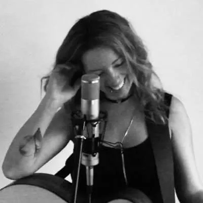 A woman smiling while singing and playing guitar in front of a microphone, capturing the essence of live music performance an