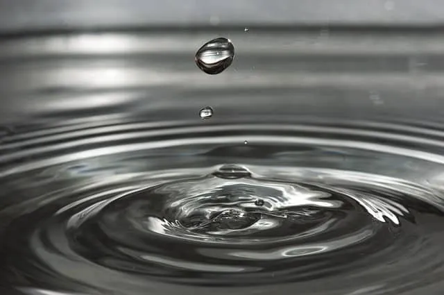Droplet falling into water creating ripples and splash, close-up black and white image of liquid dynamics, macro shot of wate