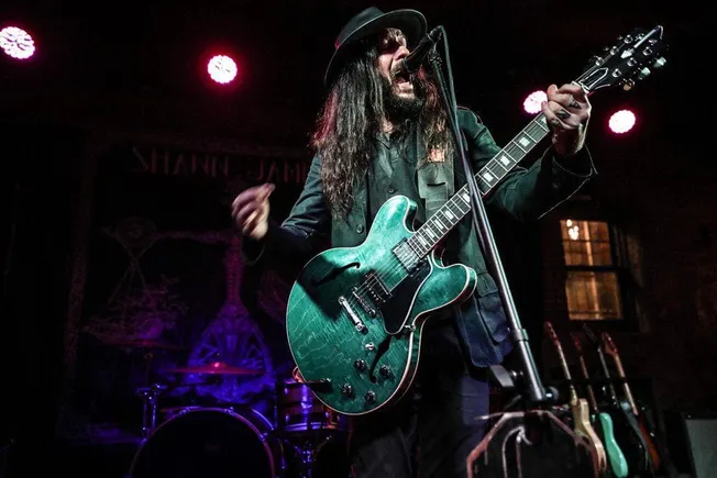 Vibrant live music performance featuring a guitarist singing into a microphone at a concert venue, illuminated by colorful st