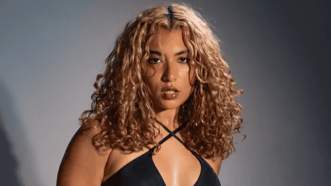 Hip hop artist woman with curly hair in black outfit posing for music photo at Hypebot event.