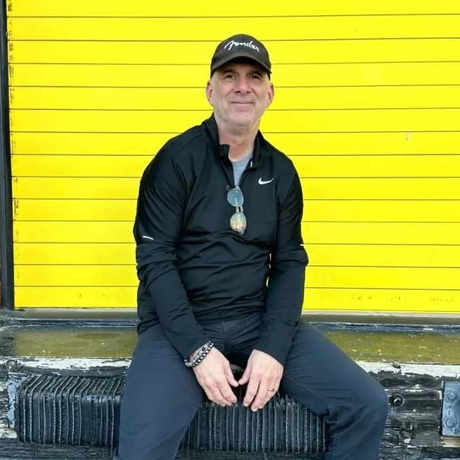 Famous man in black athletic wear sitting against bright yellow background, promoting music industry insights on Hypebot.