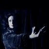 Dark-haired woman in a black cloak extending her hand in a moody, atmospheric forest scene, capturing themes of mystery, magi