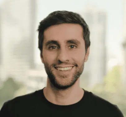 Professional male with dark hair and beard, smiling in an urban cityscape background, representing music industry news, digit
