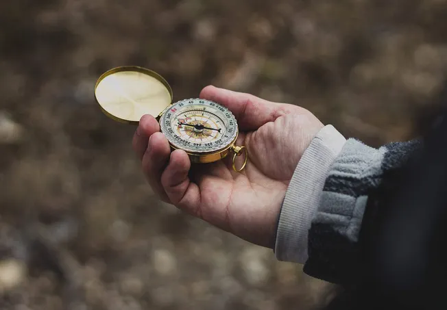 Compass held by a person outdoors, symbolizing navigation and direction.