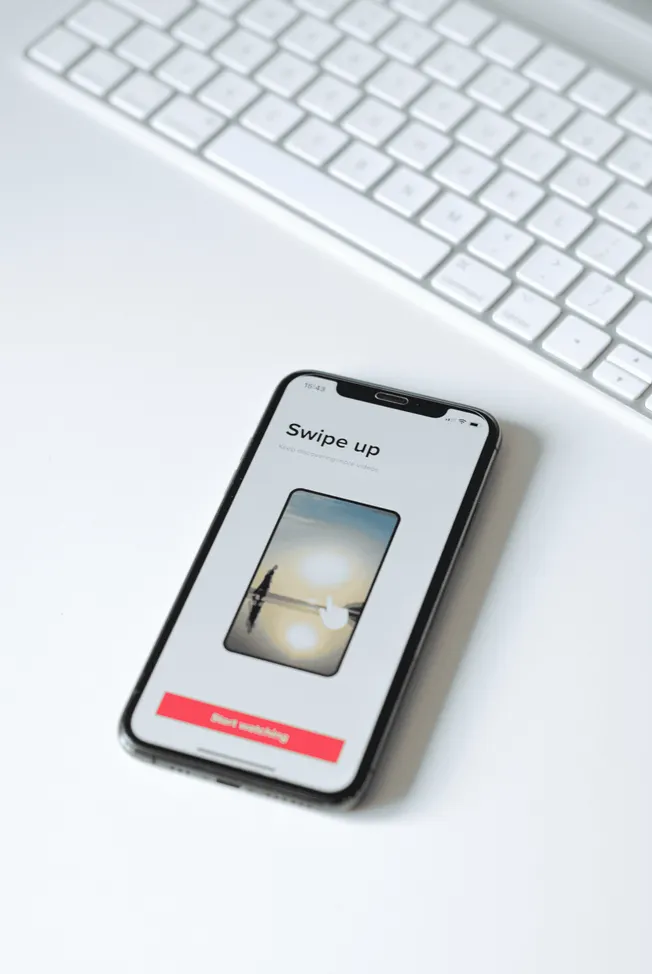 Screenshot of a smartphone displaying a swipe-up video feature on a white desk with a keyboard in the background, illustratin