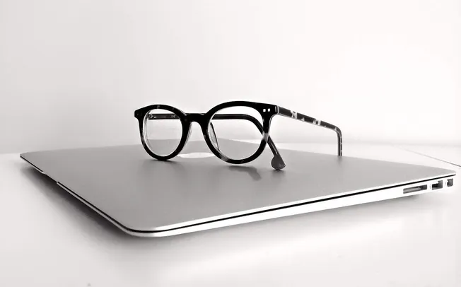 Black and white image of eyeglasses resting on a closed laptop, symbolizing technology and eyewear fashion.