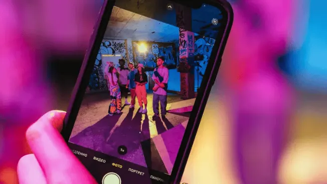 Colorful urban art scene captured on smartphone camera, featuring a group of people in graffiti-covered space with vibrant li