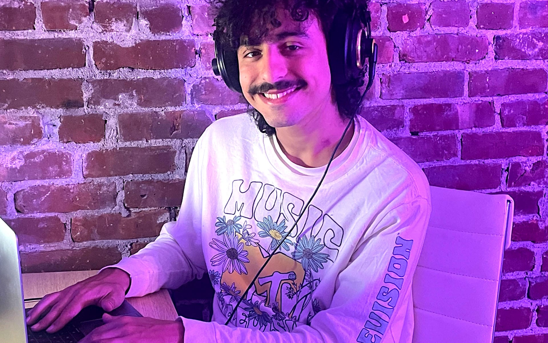 Tavi Kaye is pictured at a computer, listening to music on his headphones.