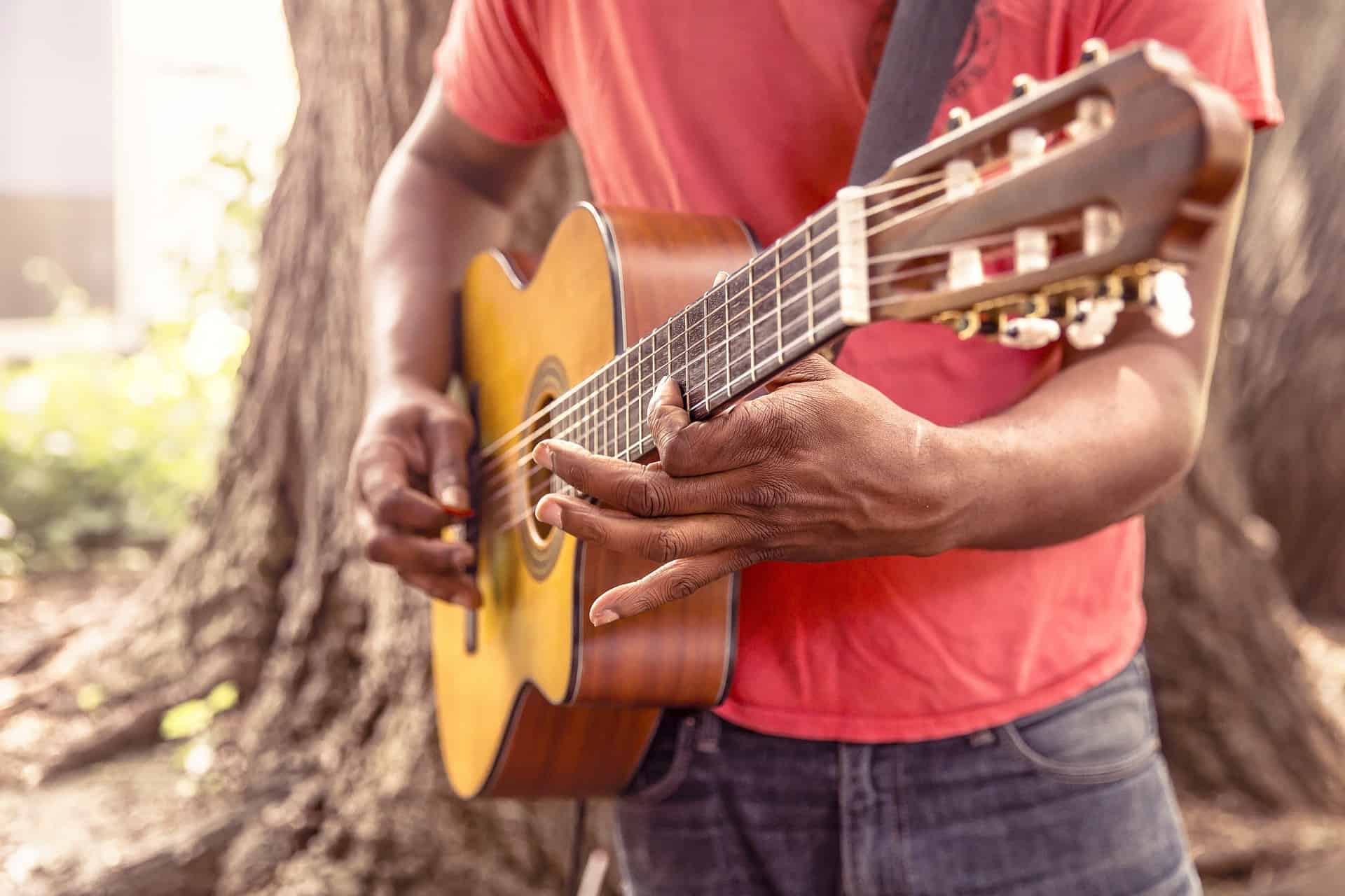 Guitar player outdoors holding acoustic guitar in a natural setting, showcasing musical expression and craftsmanship. Perfect for content related to music, guitar playing, outdoor performances, and artistic creativity.