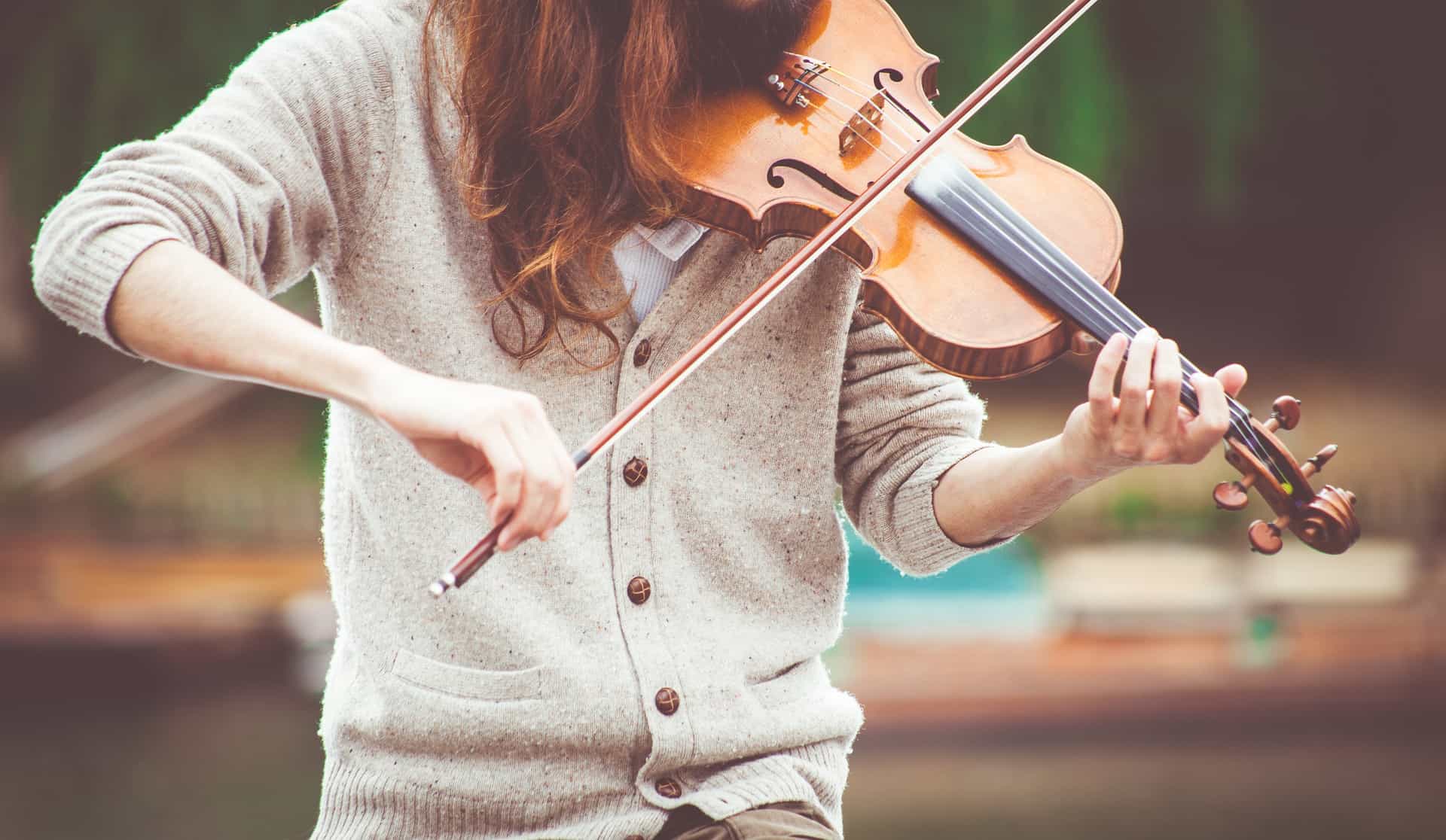 Vibrant woman playing the violin outdoors, showcasing musical passion and skill, with a blurred natural background perfect for music and art SEO relevance.