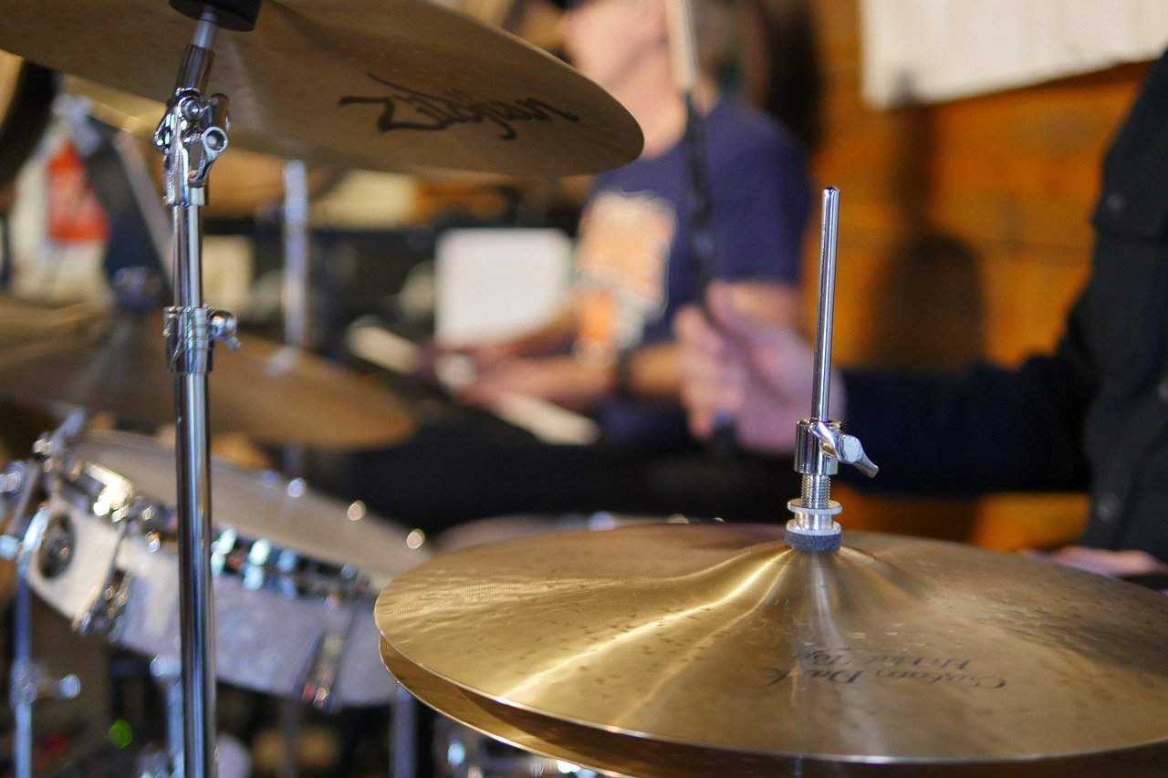 Close-up of a shiny drum cymbal with a blurred musician in the background, capturing a live musical performance setting.