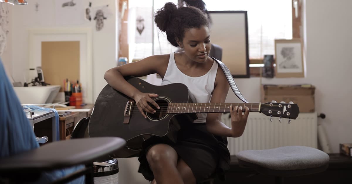 Creative young woman playing acoustic guitar in a cozy home studio, showcasing music practice, songwriting, and artistic passion. Ideal for content on music education, guitar skills, and home music setups.