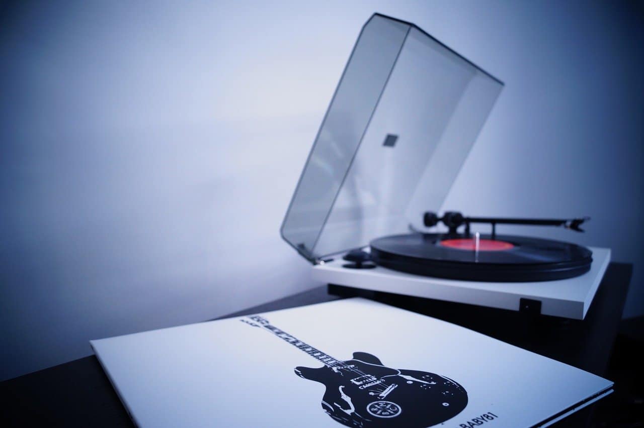 Turntable with a clear cover and a vinyl record, music artwork, and an electric guitar poster on a black table, music production, DJ setup, and musical instrument elements, music industry, Hypebot.