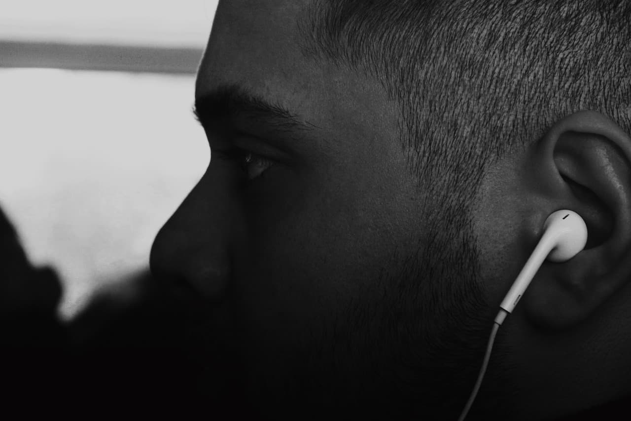 Close-up of a young man wearing earphones, listening to music or a podcast, in black and white.