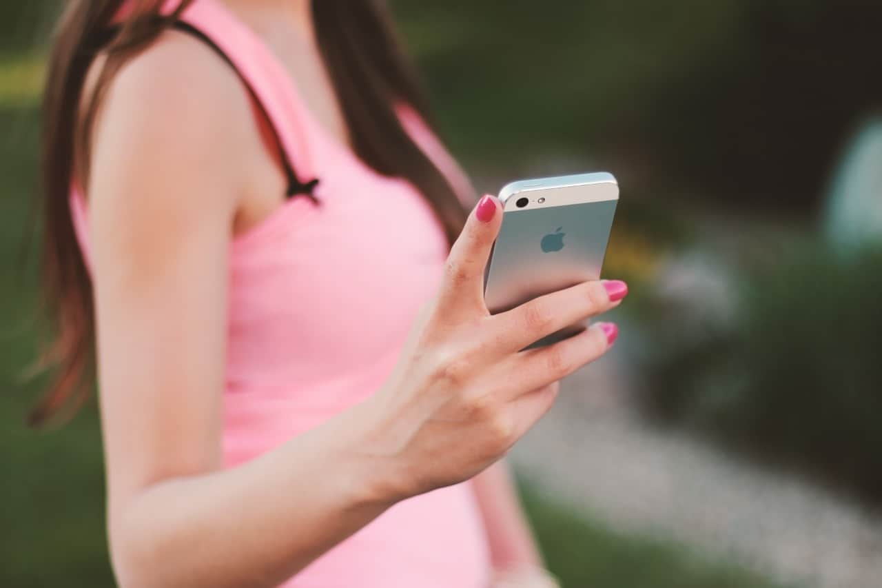 Iphone woman holding smartphone in outdoor setting, close-up of hand and device, pink dress, technology, mobile device, social media, communication, modern lifestyle, apple iPhone.
