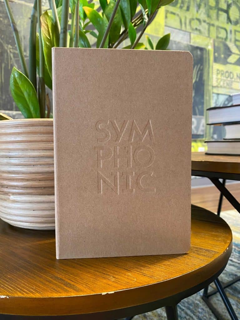 Symphonic Notebook on wooden table with greenery in background, ideal for music industry branding, mood boards, and creative projects. Perfect for musicians, composers, and music enthusiasts.