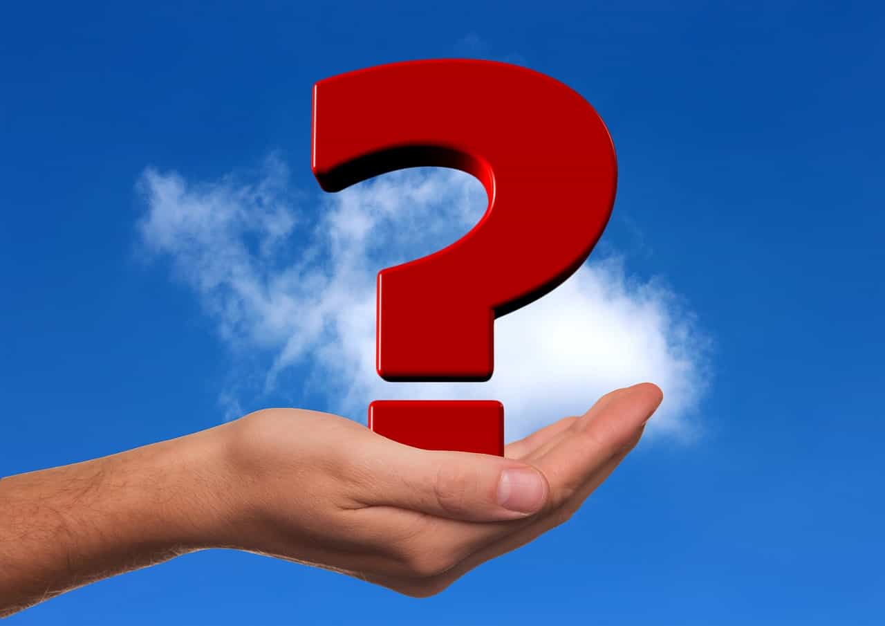 Question mark symbol held by a hand under a blue sky with clouds, representing uncertainty or inquiry.