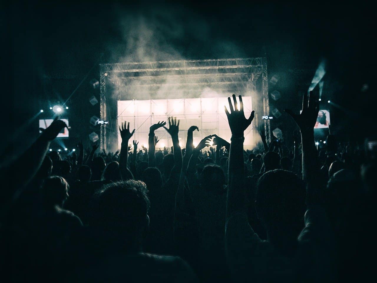 Crowd at concert with hands raised, stage with bright lights, and music festival atmosphere, emphasizing live music, entertainment, and event experience.