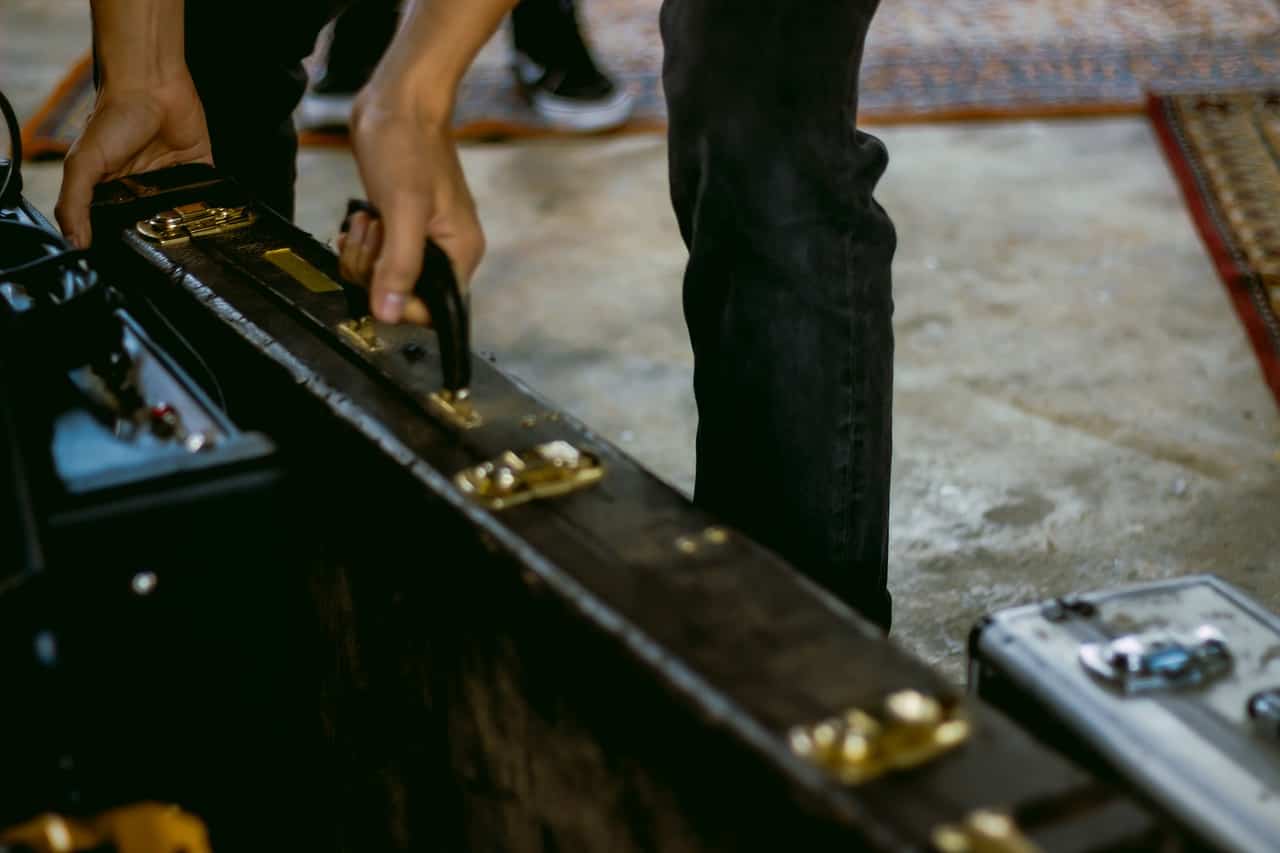 Hand lifting a vintage guitar pedalboard with gold-plated effects and pedals for music production and live performance.