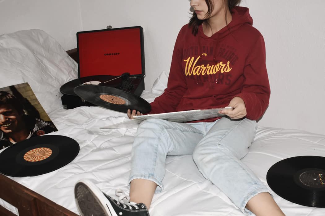 Vintage vinyl record player playing music on a bed with a woman in casual clothing, creating a cozy, retro music ambiance. Perfect for music lovers, vinyl enthusiasts, and home entertainment setups.