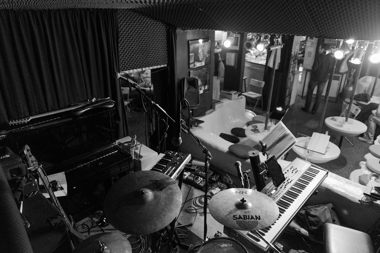 Live music performance setup with piano, drum kit, and microphones in a cozy venue. Musicians prepare for a jazz or indie concert in an intimate, soundproofed stage environment.