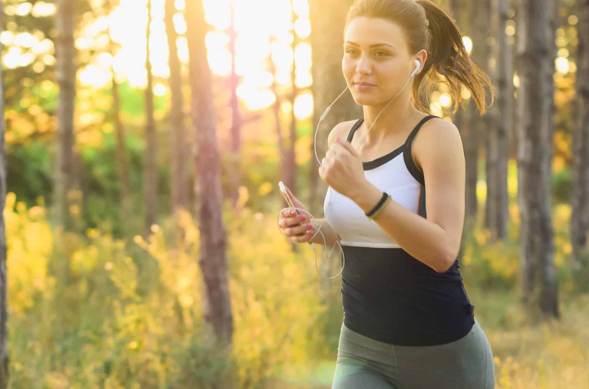 Running woman listening to music in the forest during sunset, outdoor fitness, health and wellness, exercising, nature workout, young woman, sports, active lifestyle, summer, natural light.
