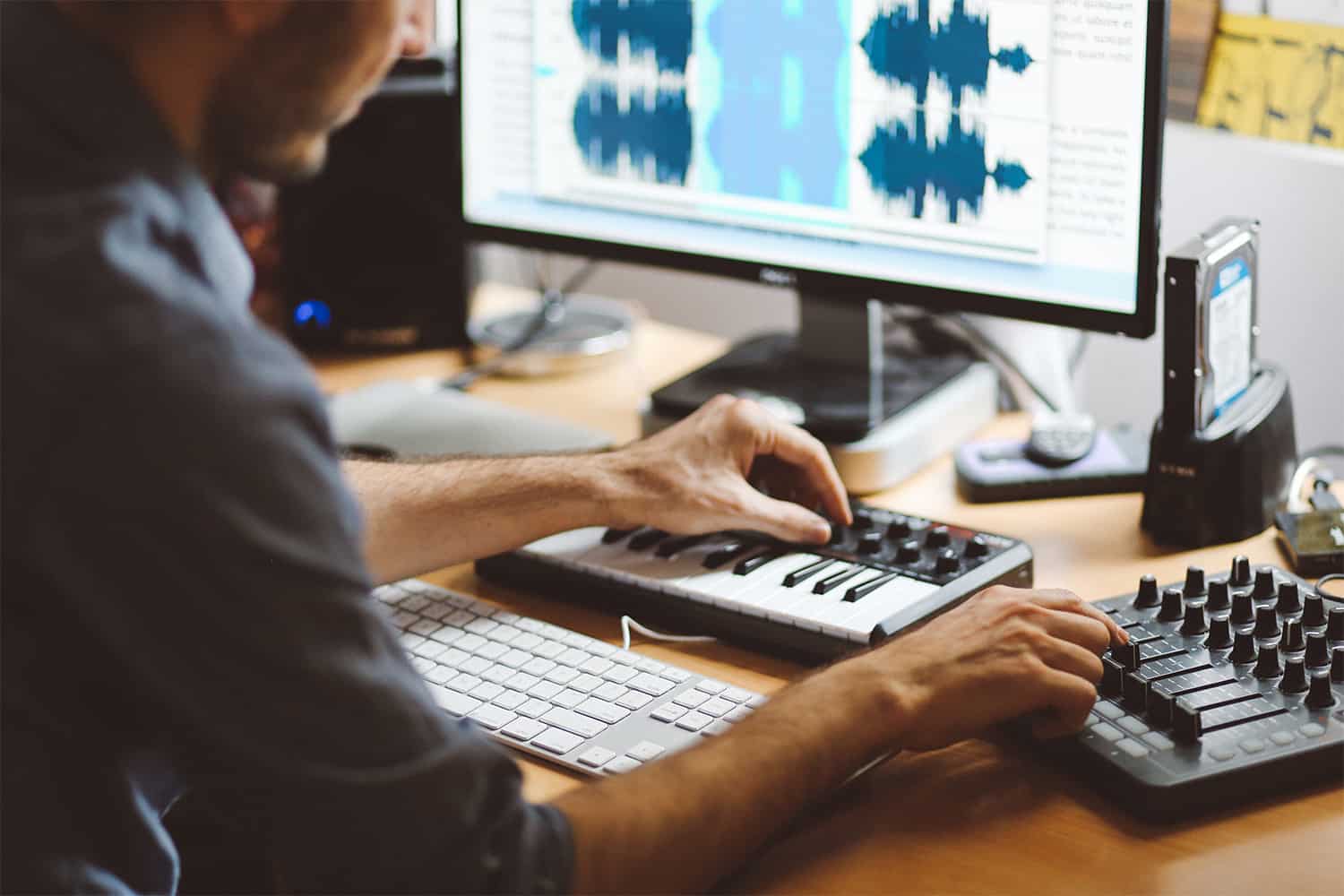 Editing music and audio production with a MIDI keyboard, audio mixer, and computer screen displaying sound waveforms, showcasing modern music creation techniques.