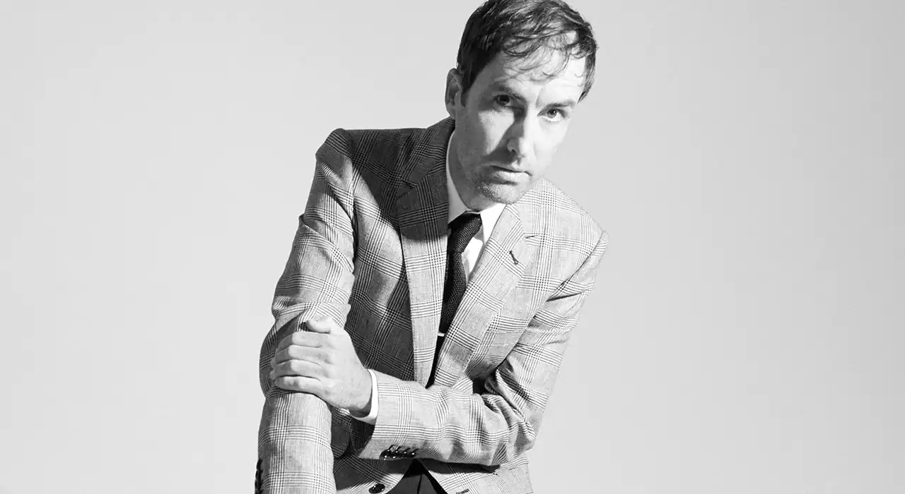 Stylish man in a checked suit with a black tie posing for a professional photoshoot, black and white image focused on music industry insights and digital marketing trends.
