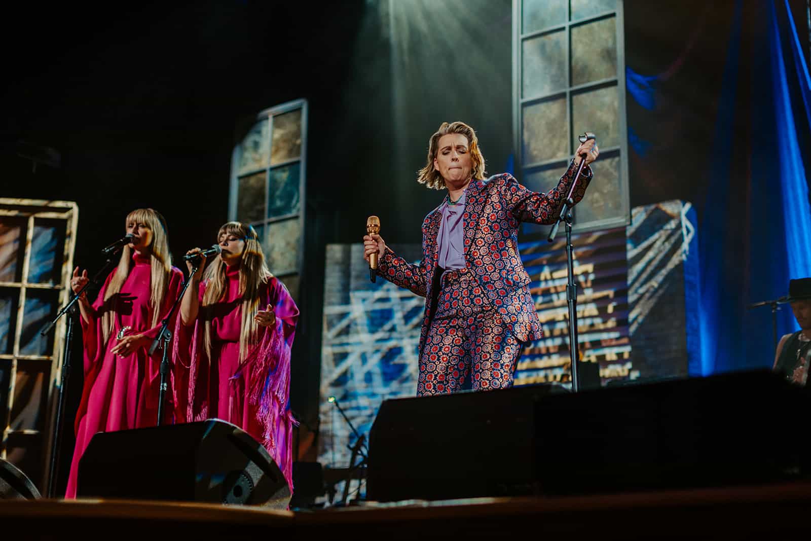 Vibrant stage performance with female singers in pink dresses and a male singer in a colorful suit, spotlighted during a live music event at Hypebot, capturing the energy of modern music and live entertainment.