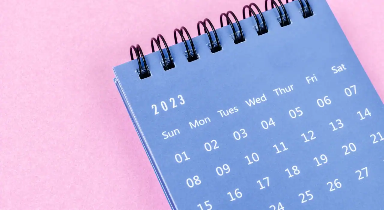 2023 calendar page on spiral-bound desk calendar with pink background.