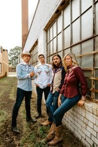 Young musicians standing outdoors against a brick building, representing modern bands and music industry trends.