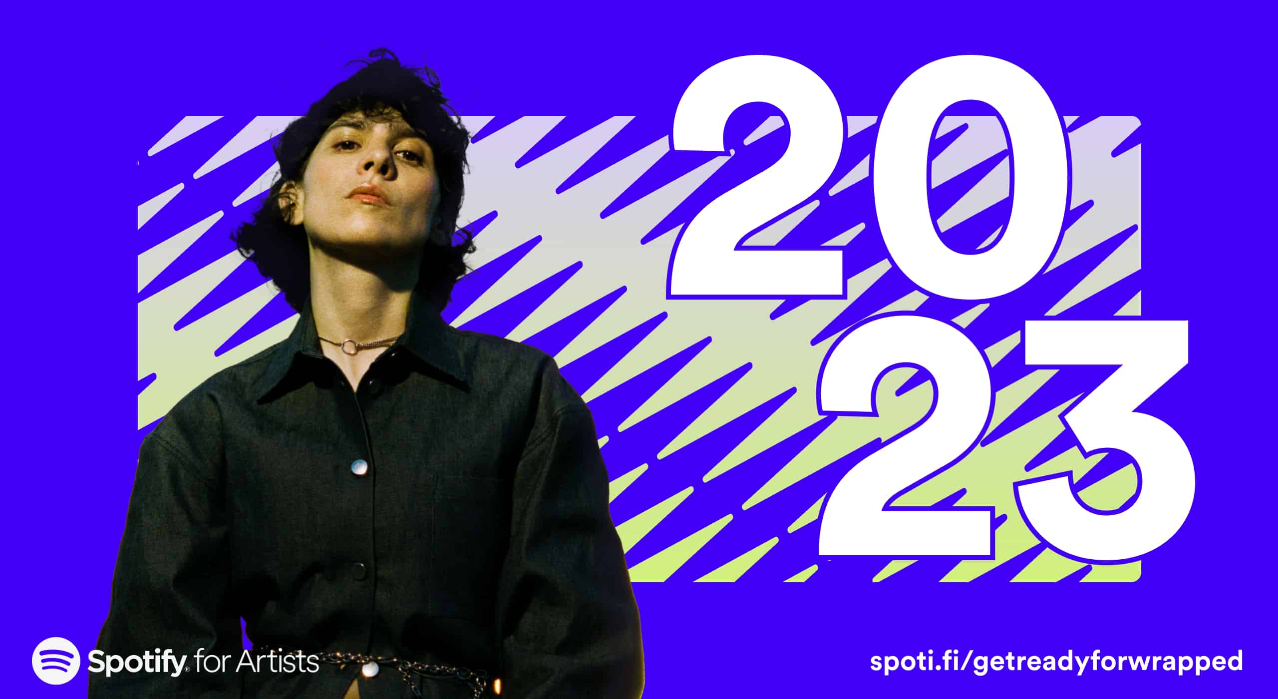 Bold woman with short dark hair in fashion-forward black outfit, promoting Spotify’s 2023 artist event with vibrant purple and lime background.
