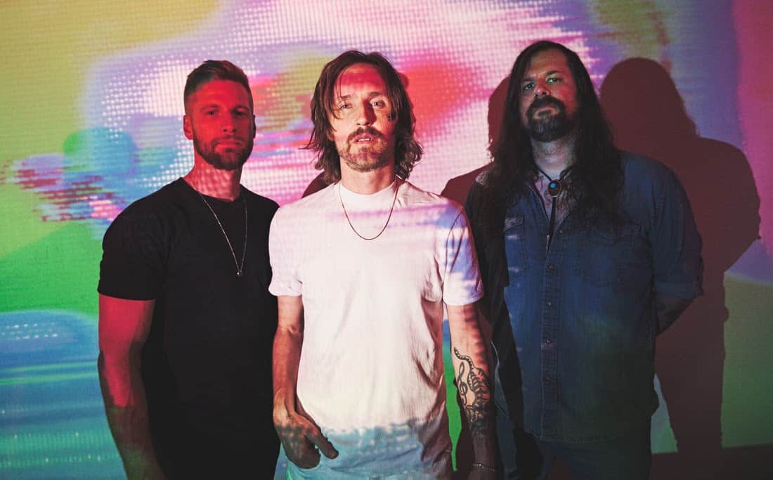 Vaporwave-inspired image of three men standing against a colorful, digital-style background with glitch effects, representing modern music culture and creativity.