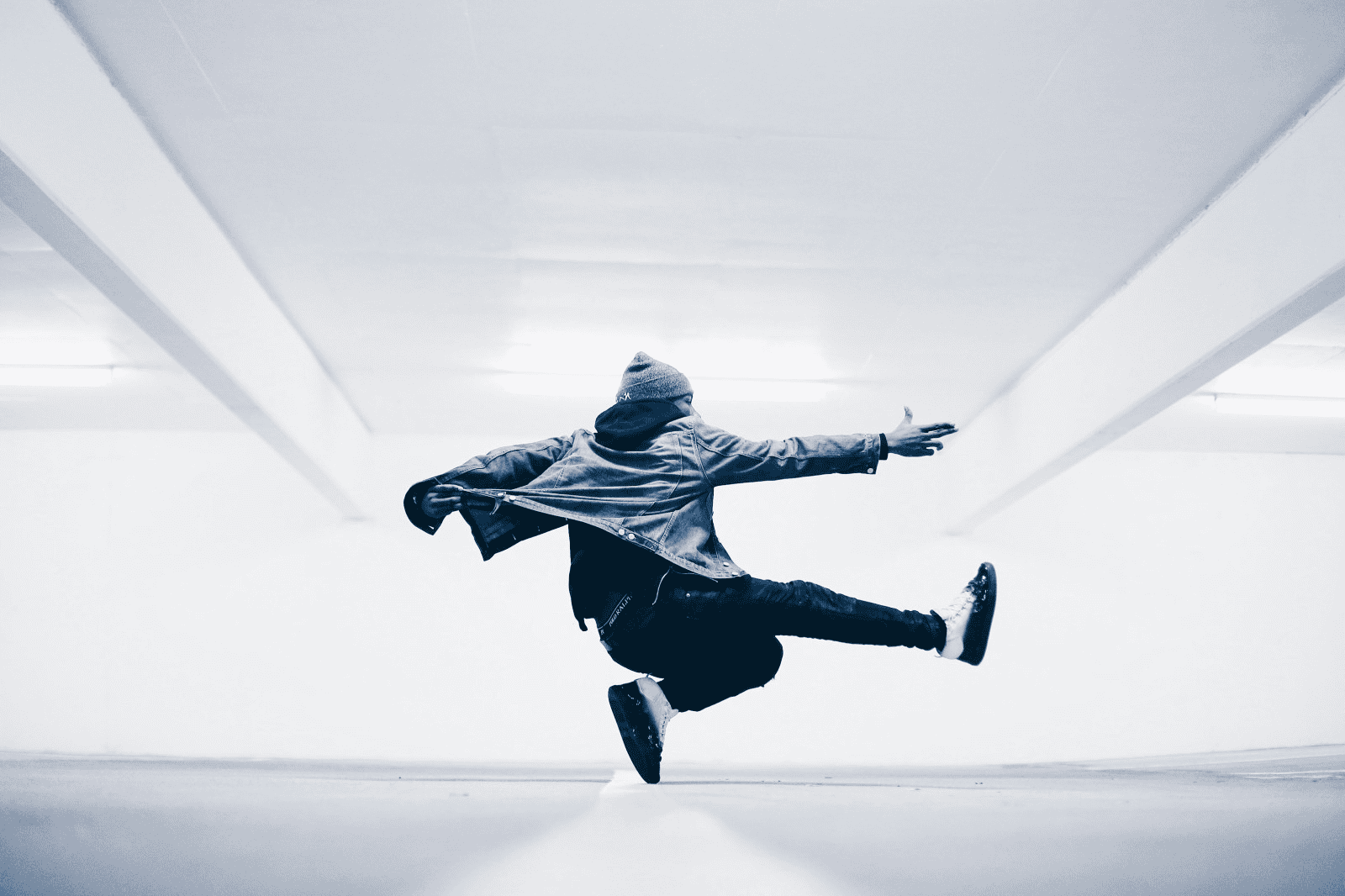 Dynamic dancer mid-air in urban parking garage, showcasing movement, street style, and energy, with a focus on dance, urban culture, and fashion for a modern, edgy aesthetic.