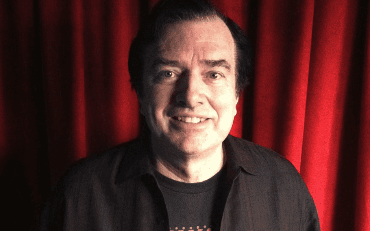 Photo of a man with dark hair smiling in front of a red curtain, music industry expert and keynote speaker at Hypebot events, promoting music marketing strategies and industry insights for artists and labels.