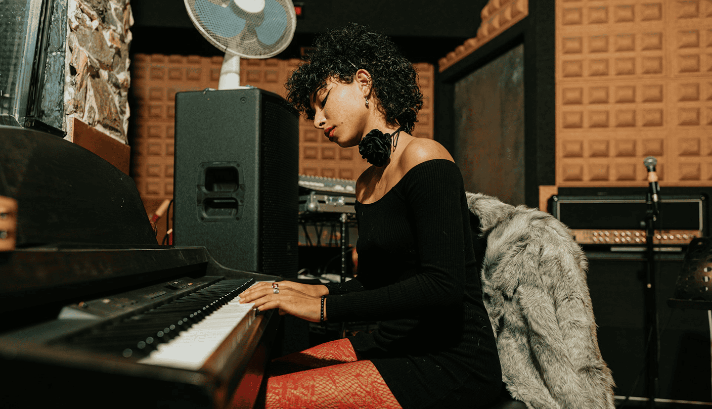 Stunning woman playing piano in a music studio with professional audio equipment and acoustic wall panels for optimal sound quality.