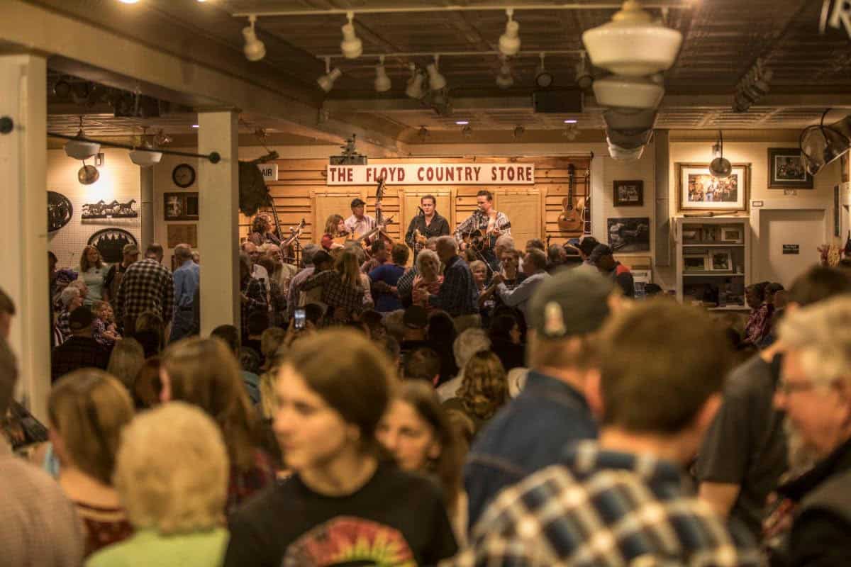 Crowd gathered at a country music event in a cozy indoor venue, live band performing on stage, wooden decor, and an energetic atmosphere at The Floyd Country Store, promoting live music and community engagement in the music industry.
