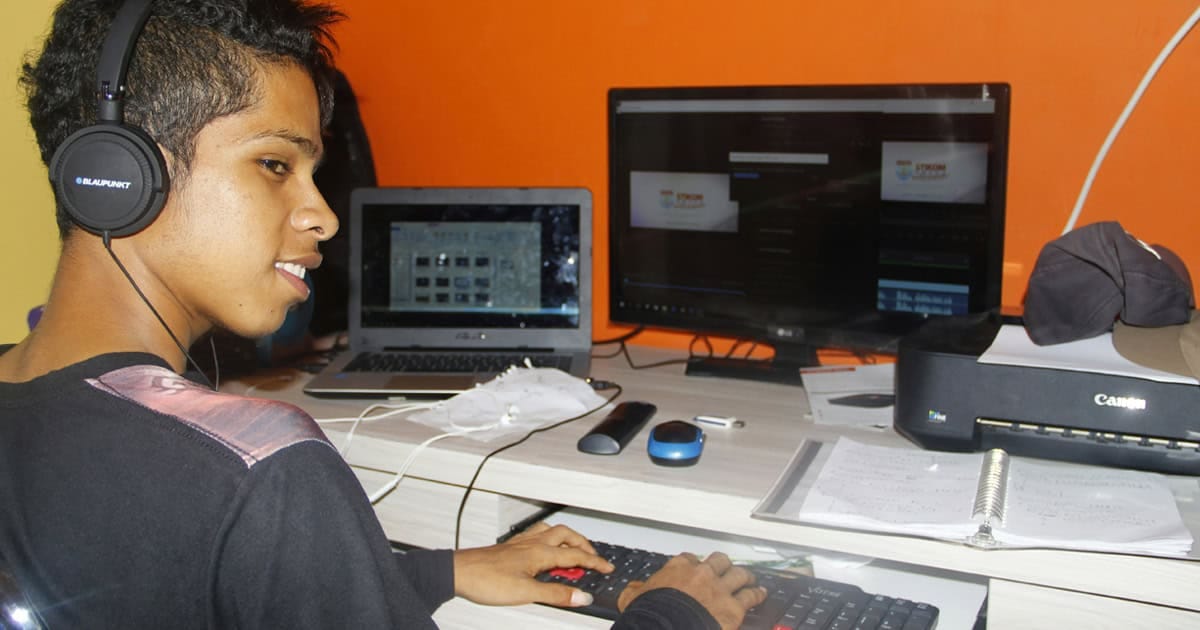 Young person wearing headphones working on a computer with multiple screens in a music production or multimedia workspace.
