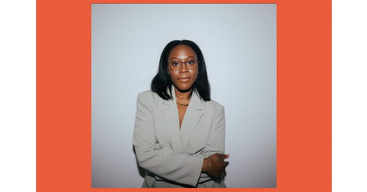 Empowered Black woman wearing glasses and a business blazer, standing confidently against a modern background. Professional portrait showcasing leadership, confidence, and diversity in the workplace.