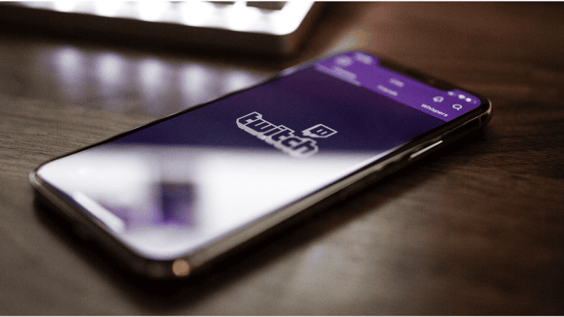 Twitch app on smartphone displaying live streaming platform interface, popular for gaming and content creation, on wooden table with blurred background.