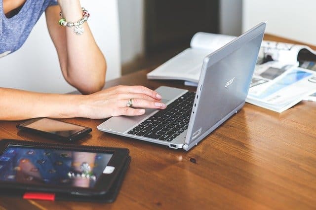 A person working on a silver laptop at a wooden desk with a smartphone and magazines nearby, demonstrating digital marketing and content creation for the music industry.