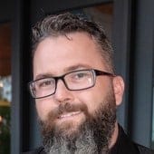 AI-generated image of a smiling man with glasses, beard, and casual attire outdoors, representing Hypebot's focus on music industry insights and digital media innovation.
