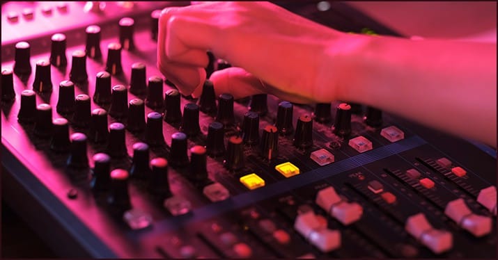 Mixing console with hand adjusting audio levels at a music event or studio, showcasing sound engineering and music production equipment.