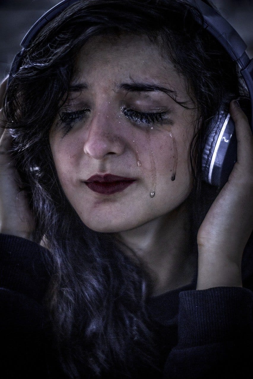 Distressed young woman with tears on her face listening to music through headphones, expressing sadness or emotional pain.