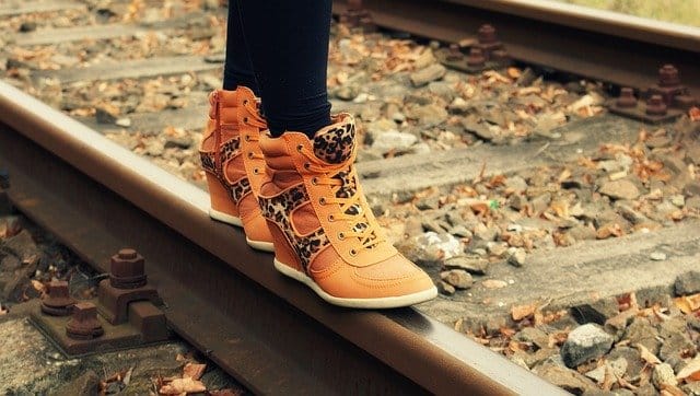 Fashionable leopard print and tan high-top sneakers worn on railway track, showcasing trendy footwear styles.