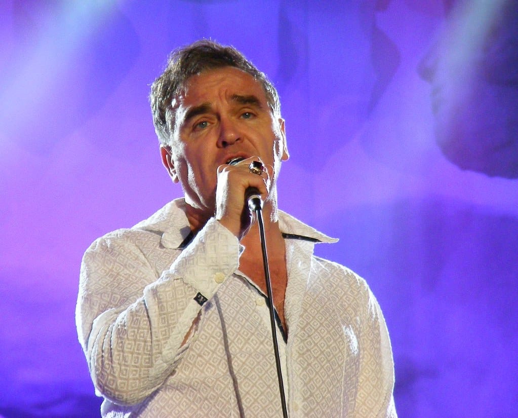 Male singer performing with microphone on stage, singing passionately, purple stage lighting, music performance, live concert atmosphere.