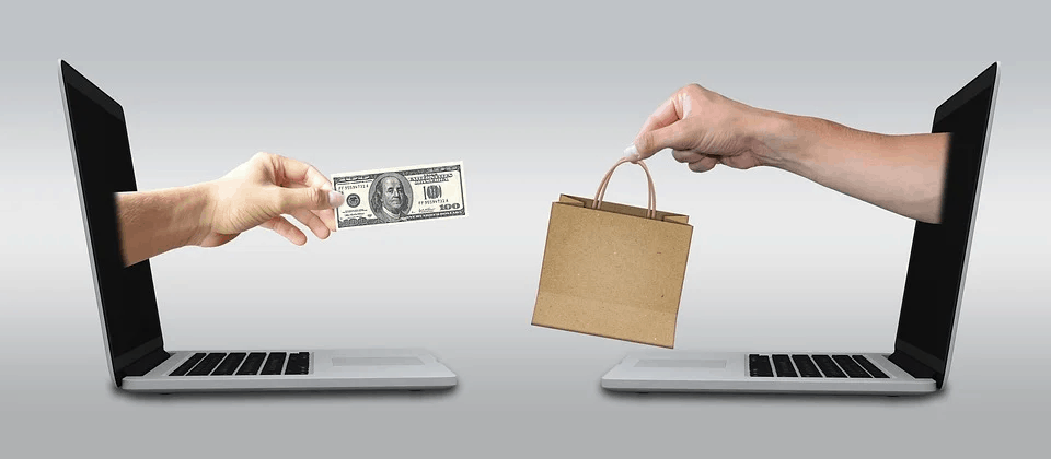 Digital commerce concept with hands exchanging money and a shopping bag through laptops.