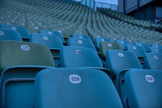 Empty stadium seats in a sports venue or concert hall, showcasing blue and green chairs arranged in rows for audience seating.