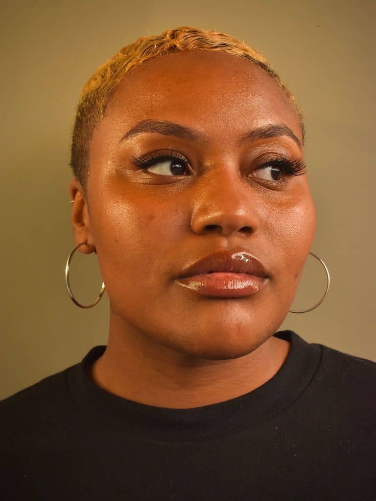 Black woman with short blonde hair and hoop earrings, close-up portrait, vibrant makeup, confident expression, modern hairstyle, fashionable look, beauty and personal style, Hypebot.