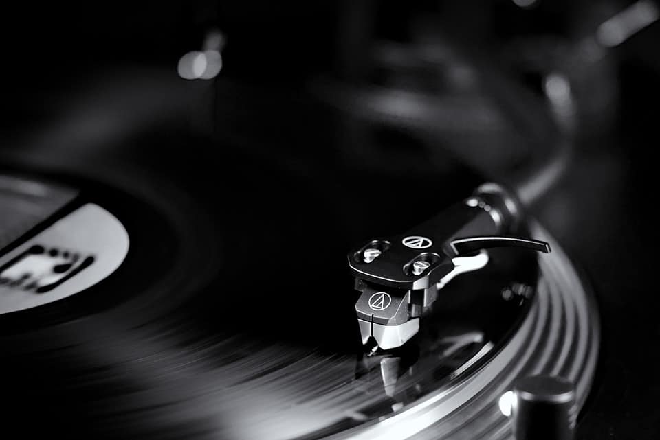 Vintage turntable stylus and record playing, music production equipment, analog audio setup, DJ equipment, high-fidelity sound system, vinyl record listening environment, black and white music gear, creative music studio, audio engineering, immersive listening experience.